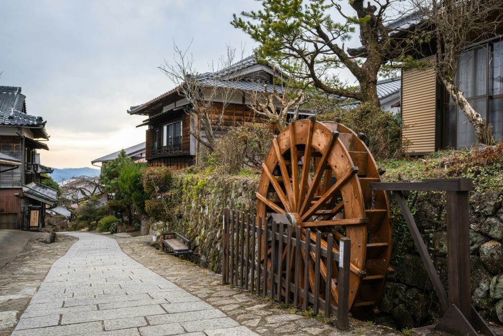 a wooden water wheel sitting on the side of a road
