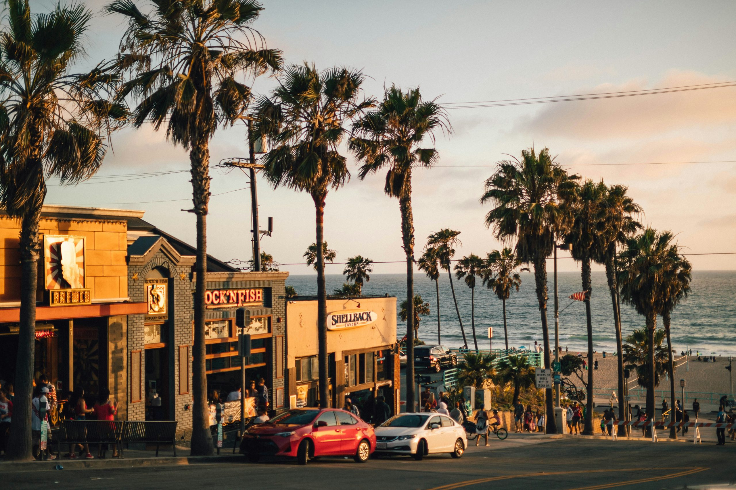 Palm-lined street of a Southern California beach town at sunset with the ocean beyond